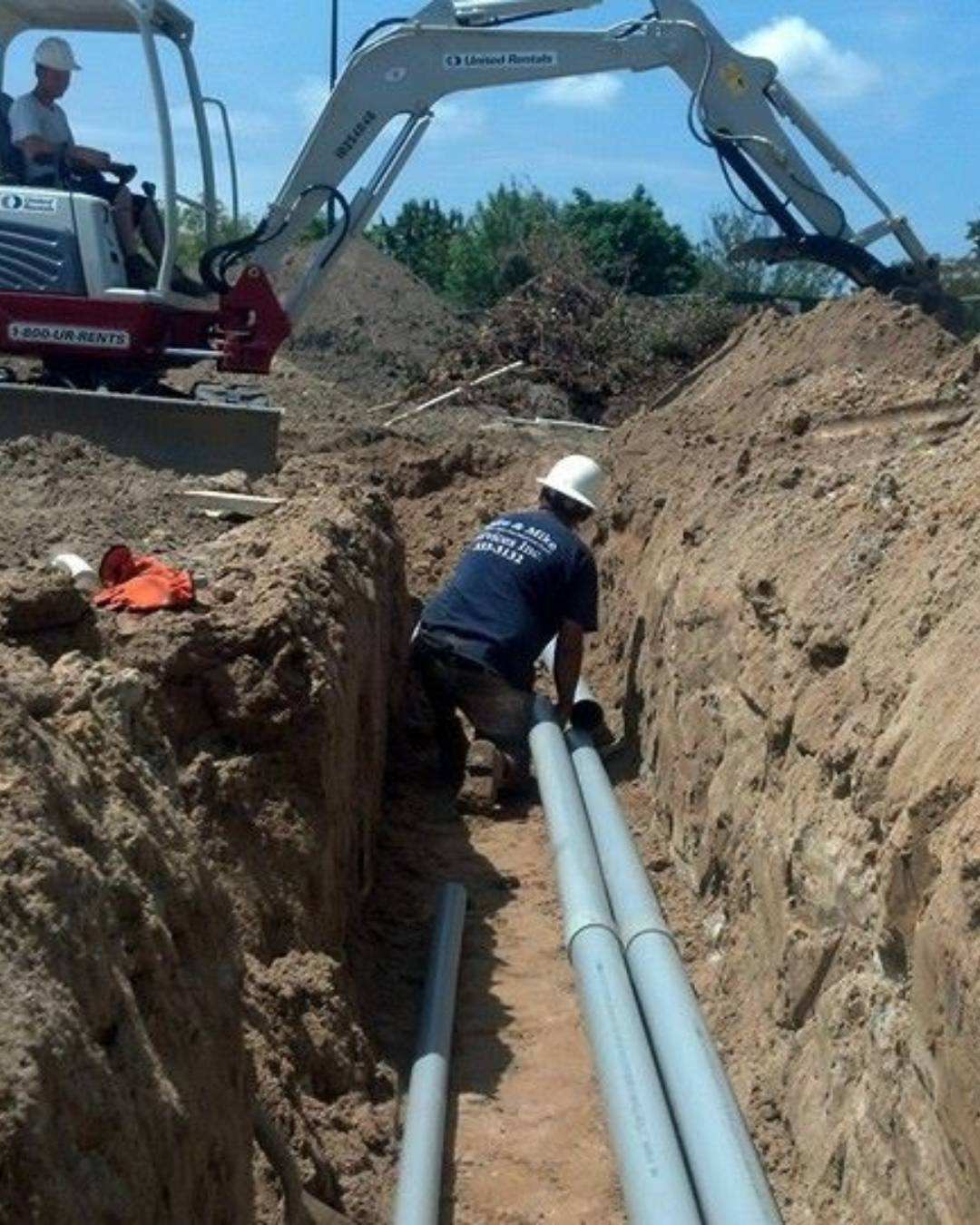 Worker Inside An Unsloped, Unshored Deep Trench Alongside Heavy Machinery